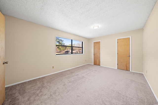 unfurnished bedroom featuring light carpet, a textured ceiling, two closets, and baseboards