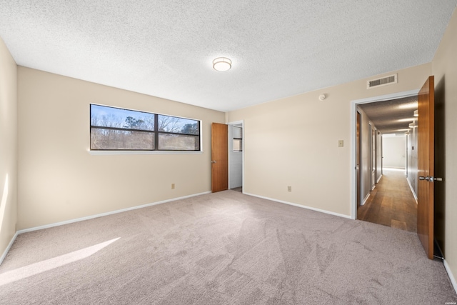 unfurnished room featuring dark colored carpet, visible vents, a textured ceiling, and baseboards