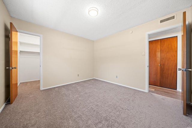 unfurnished bedroom featuring visible vents, a spacious closet, carpet flooring, a textured ceiling, and baseboards