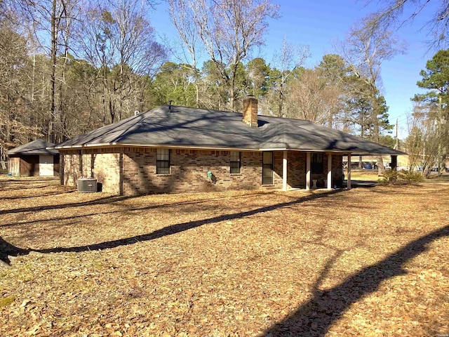 back of property with brick siding, a chimney, and central AC unit