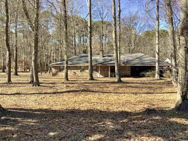 view of front facade with a chimney, a view of trees, and a carport