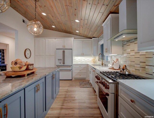 kitchen with premium appliances, white cabinets, vaulted ceiling, a sink, and wall chimney range hood