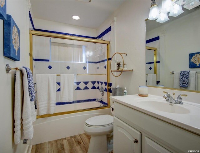 full bath featuring enclosed tub / shower combo, vanity, toilet, and wood finished floors