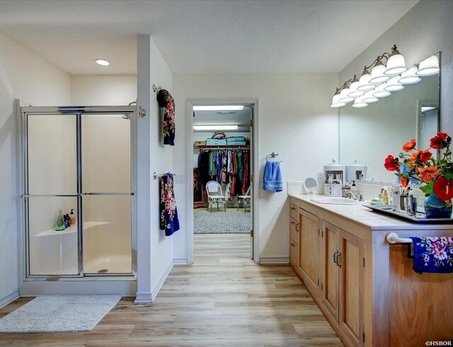 bathroom with baseboards, wood finished floors, a walk in closet, vanity, and a shower stall