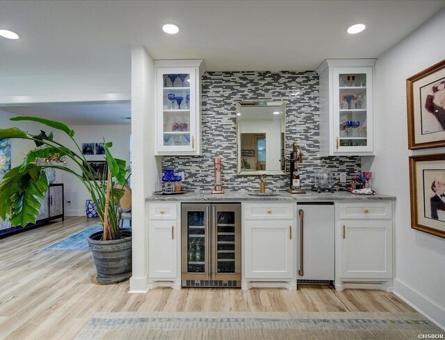 bar with wine cooler, refrigerator, indoor wet bar, tasteful backsplash, and light wood-style flooring