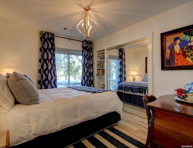 bedroom with a closet, wood finished floors, visible vents, and an inviting chandelier