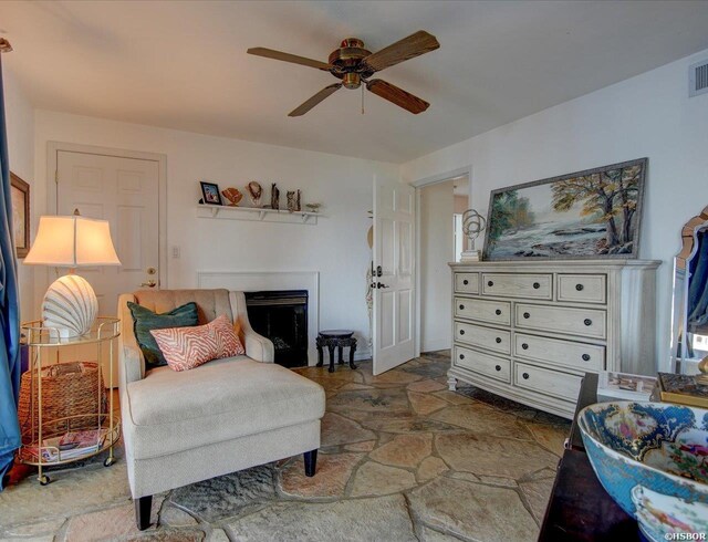 sitting room featuring stone finish flooring, a fireplace, and ceiling fan