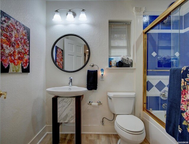 bathroom featuring enclosed tub / shower combo, toilet, a sink, wood finished floors, and baseboards