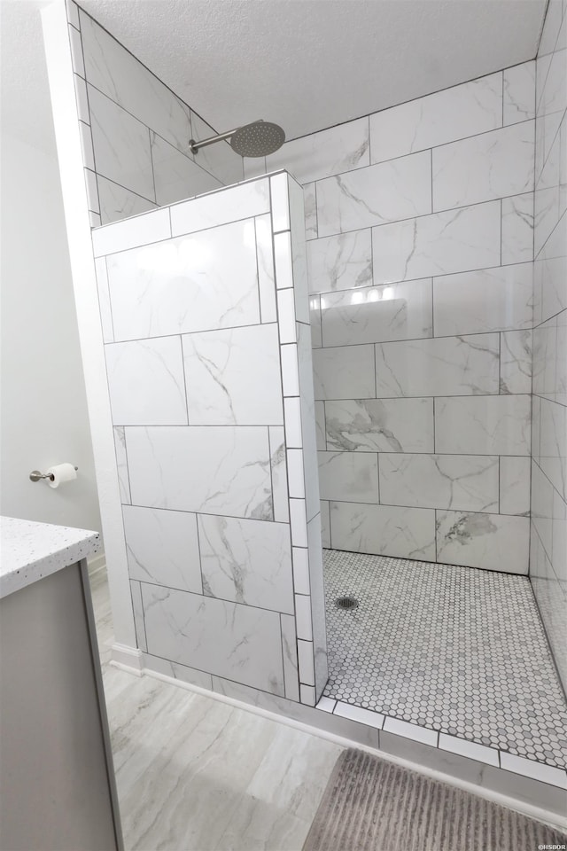 full bathroom featuring a textured ceiling, marble finish floor, vanity, and a walk in shower