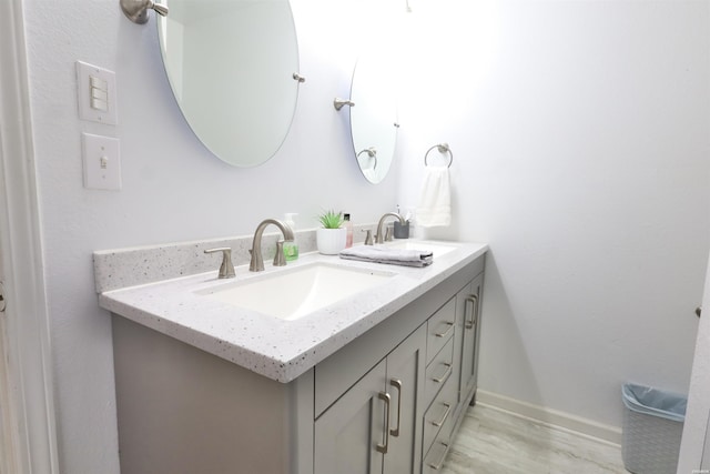 bathroom featuring double vanity, wood finished floors, baseboards, and a sink