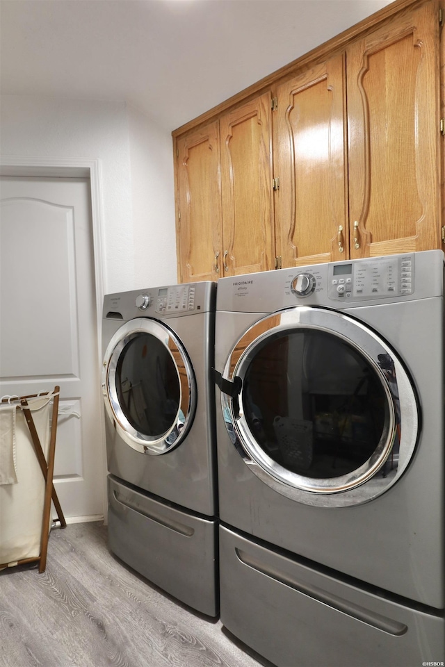 laundry room with washing machine and dryer, cabinet space, and light wood-style floors