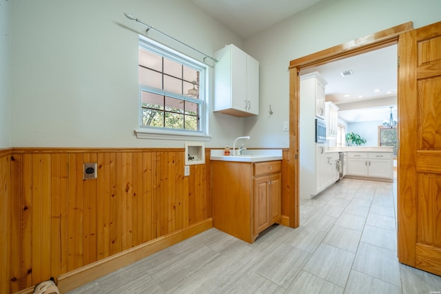 laundry area featuring cabinet space, visible vents, wainscoting, wood walls, and a sink