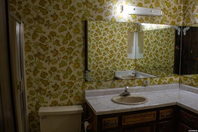 bathroom with vanity, toilet, and wallpapered walls