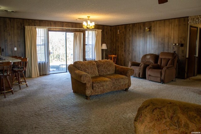 living area featuring carpet floors, wood walls, a notable chandelier, and a textured ceiling