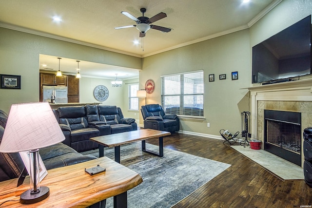 living room with baseboards, a ceiling fan, a tiled fireplace, hardwood / wood-style flooring, and crown molding