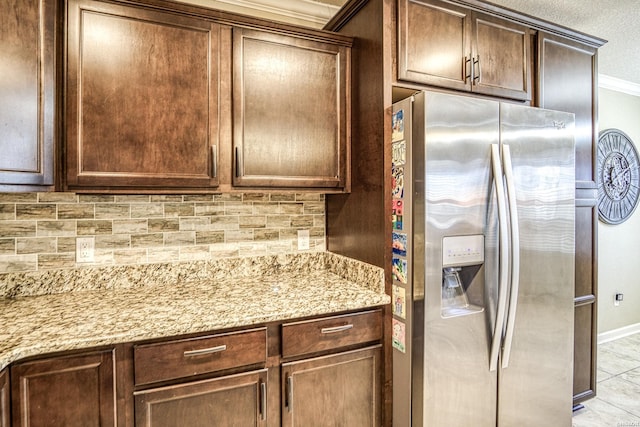 kitchen featuring light stone counters, dark brown cabinetry, baseboards, tasteful backsplash, and stainless steel fridge