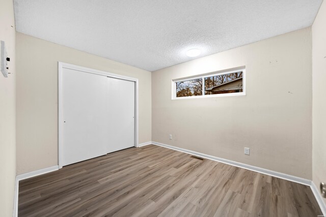 unfurnished bedroom with a closet, a textured ceiling, baseboards, and wood finished floors