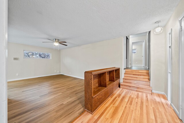 empty room with light wood-style floors, baseboards, a ceiling fan, and a textured ceiling