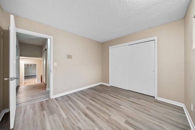 unfurnished bedroom with a textured ceiling, a closet, light wood-type flooring, and baseboards