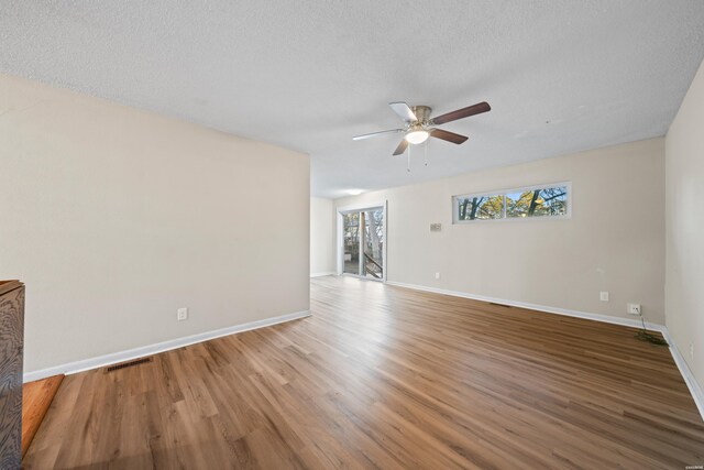 unfurnished living room featuring a textured ceiling, wood finished floors, visible vents, and baseboards