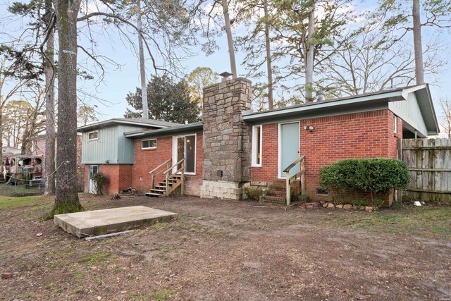 rear view of property featuring entry steps, brick siding, fence, and a chimney