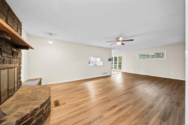 living area featuring light wood-type flooring, visible vents, a fireplace, and a textured ceiling