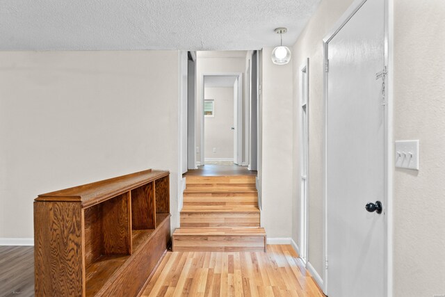 hall with a textured ceiling, baseboards, and wood finished floors