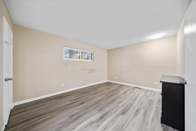 unfurnished room featuring light wood-style floors, baseboards, and a textured ceiling