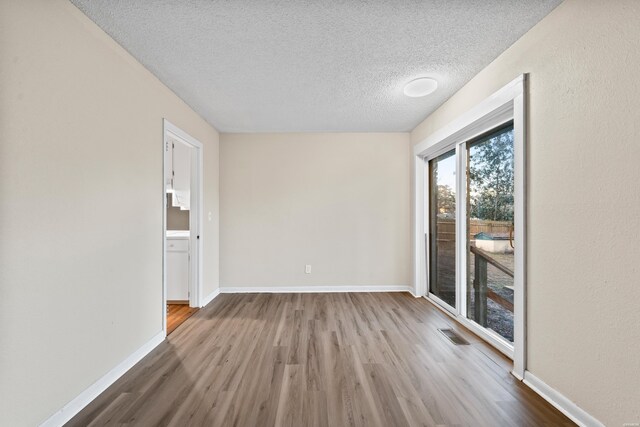 unfurnished room featuring visible vents, a textured ceiling, baseboards, and wood finished floors