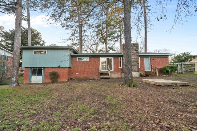 rear view of house with entry steps, brick siding, fence, and a chimney