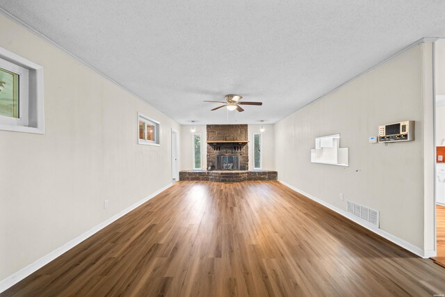 unfurnished living room featuring a textured ceiling, a fireplace, wood finished floors, visible vents, and a ceiling fan