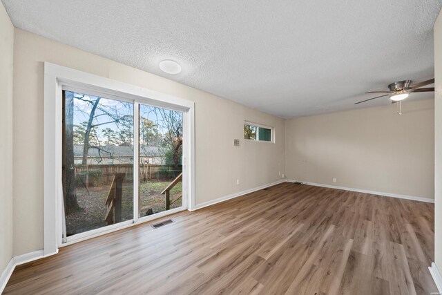 unfurnished room with a textured ceiling, wood finished floors, and a wealth of natural light