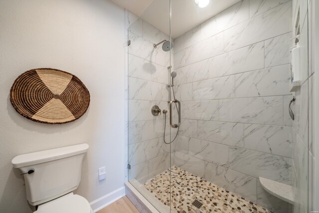 bathroom with toilet, a stall shower, baseboards, and wood finished floors