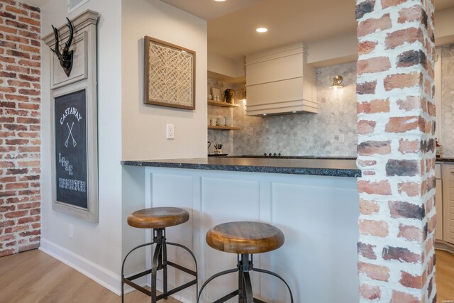 kitchen featuring tasteful backsplash, dark countertops, cream cabinetry, light wood-style floors, and open shelves