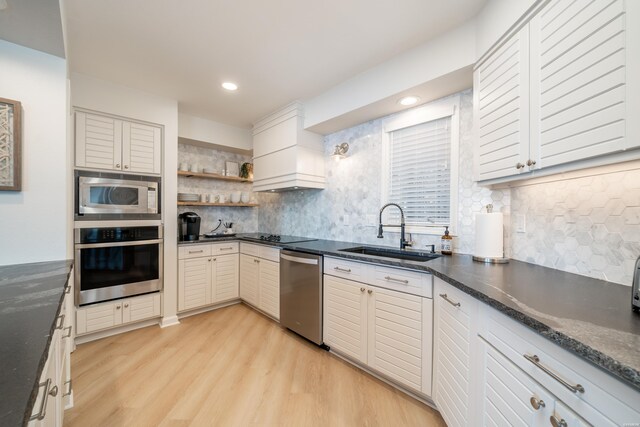 kitchen featuring stainless steel appliances, open shelves, dark countertops, and a sink