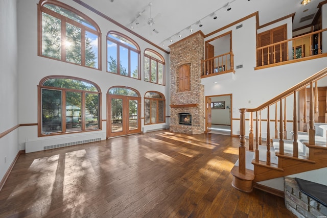 69 Resplandor Way, Hot Springs Village, AR 71909 - unfurnished living room with a towering ceiling, a brick fireplace, rail lighting, wood-type flooring, and visible vents