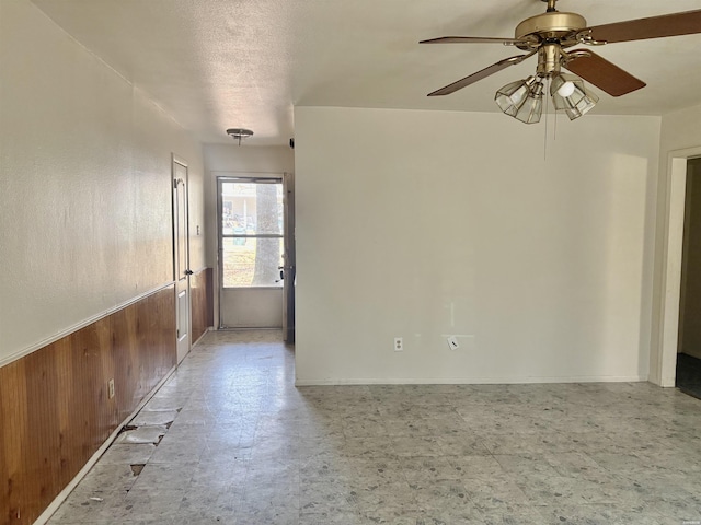 empty room with a wainscoted wall, ceiling fan, wooden walls, and light floors