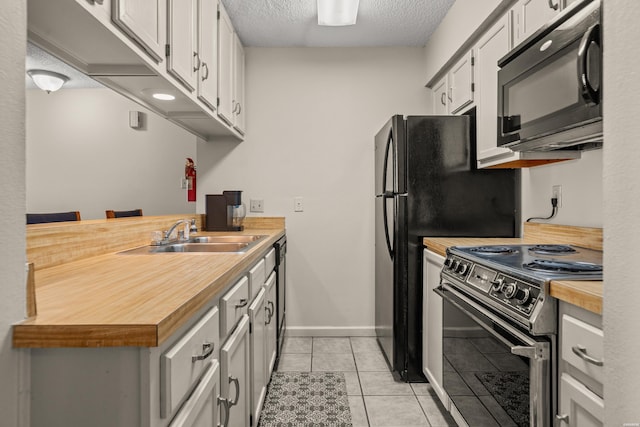 kitchen featuring light tile patterned floors, electric stove, butcher block countertops, black microwave, and a sink