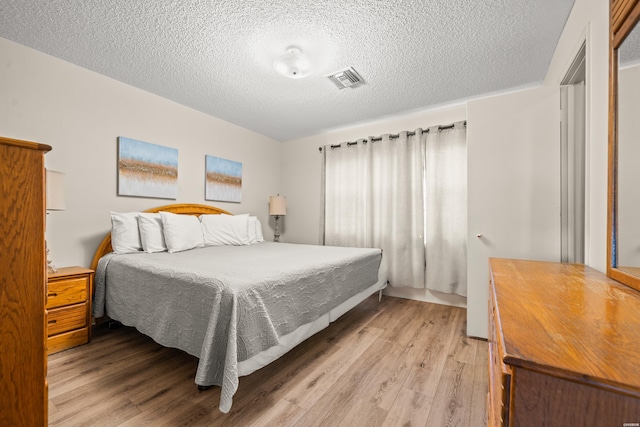 bedroom with visible vents, a textured ceiling, and light wood finished floors