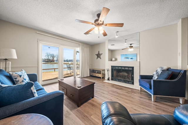 living room featuring light wood-type flooring, a water view, a textured ceiling, and a tiled fireplace