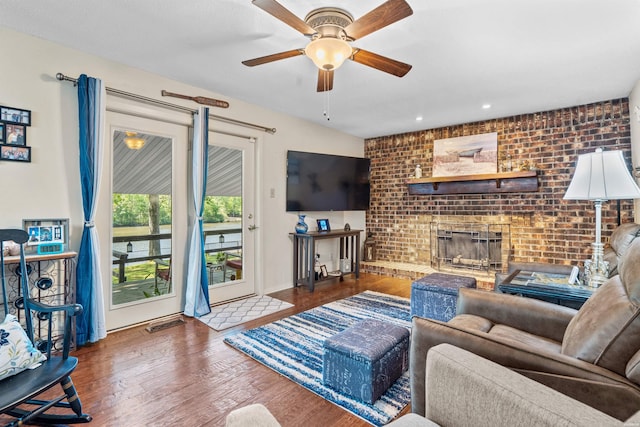 living room with a brick fireplace, brick wall, and wood finished floors