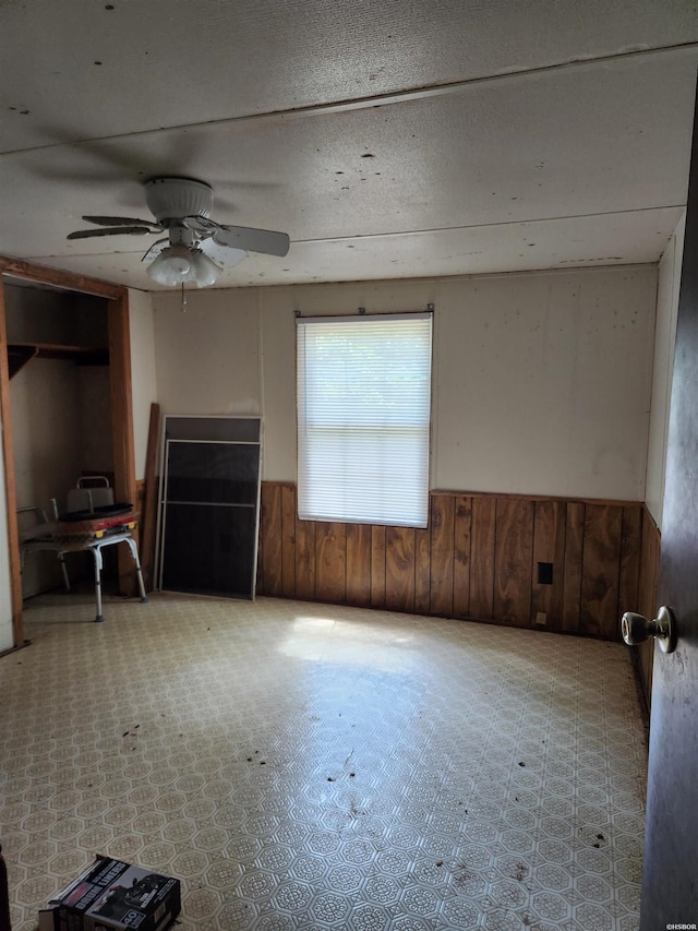 256 Shawnee Loop, Amity, AR 71921 - unfurnished living room featuring wainscoting, ceiling fan, and wood walls