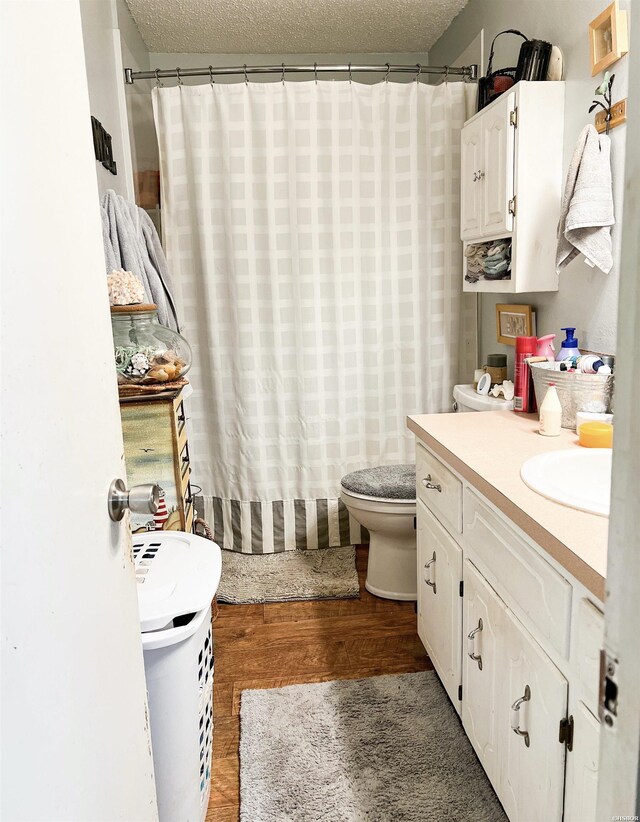 full bath with a shower with curtain, vanity, a textured ceiling, and wood finished floors