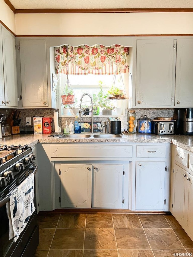 kitchen featuring tasteful backsplash, light countertops, a sink, and black gas stove