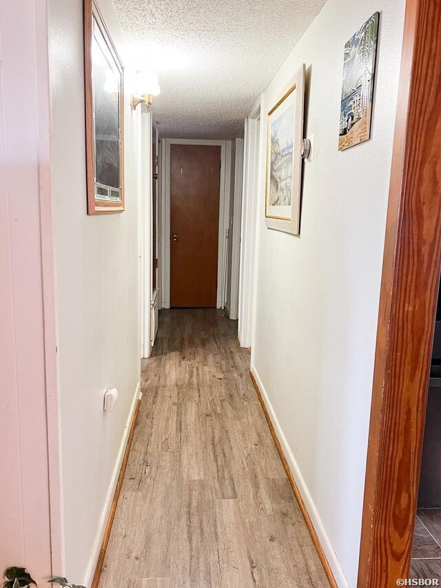 corridor with light wood-style floors, baseboards, and a textured ceiling