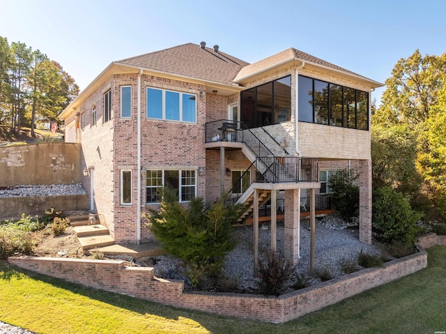 back of property featuring brick siding, a shingled roof, a sunroom, stairs, and a yard