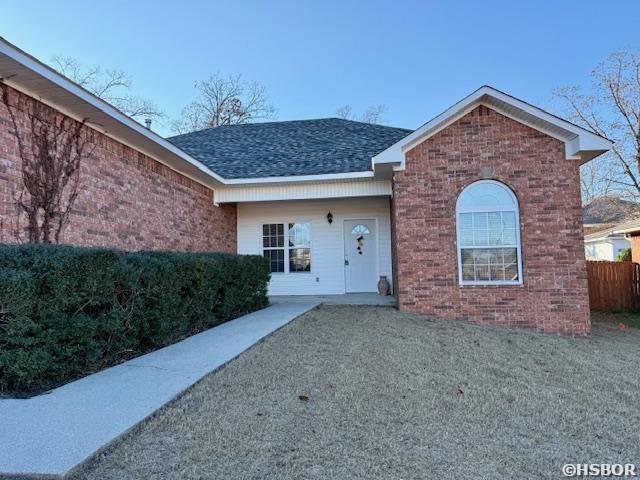 view of front of home featuring a shingled roof, fence, a front lawn, and brick siding