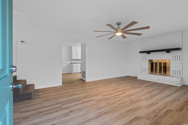 unfurnished living room with light wood-type flooring, a brick fireplace, visible vents, and a ceiling fan