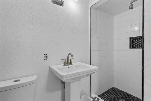 bathroom featuring a sink, a textured wall, a shower stall, and toilet