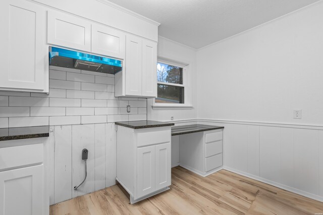 kitchen with a wainscoted wall, light wood finished floors, white cabinets, dark stone countertops, and under cabinet range hood